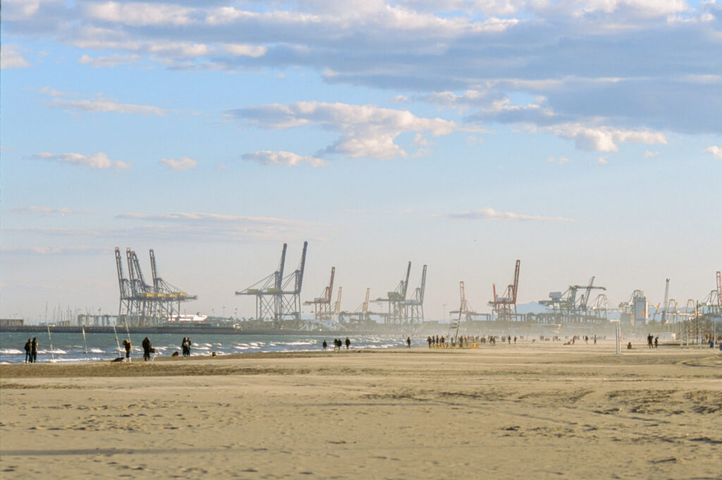 people walking beach valencia winter spain scene with industrial port container cranes